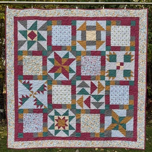 May include: A quilt with a patchwork design featuring various geometric shapes and patterns in shades of red, green, brown, and white.