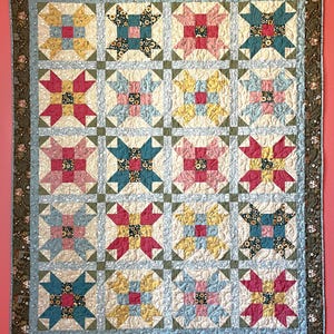 May include: A rectangular patchwork quilt featuring a grid of sixteen star-shaped blocks. Each block contains a central floral square surrounded by four pointed petals in shades of pink, yellow, and teal. The quilt has a dark green border.