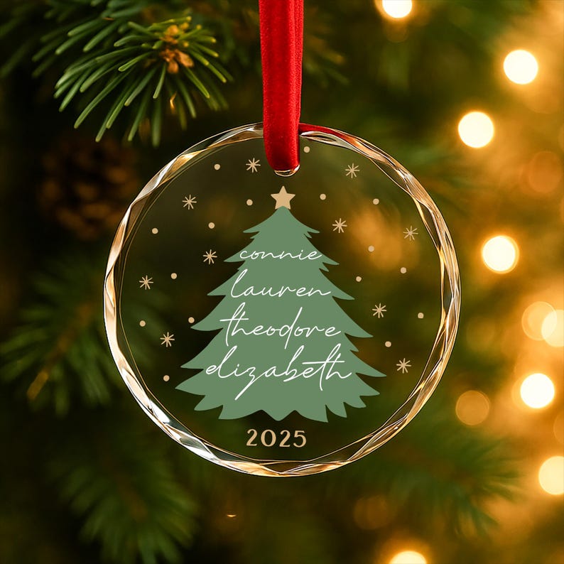 May include: A clear, round Christmas ornament with a red ribbon. The ornament features a green Christmas tree design with names and the year 2025. Snowflakes and a star are also included in the design.