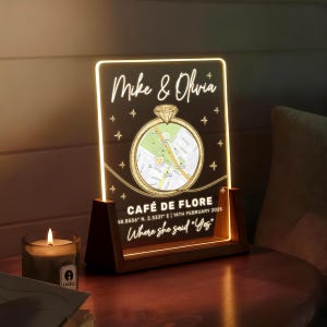 May include: A personalized illuminated sign with the names "Mike & Olivia" and a map of "Café de Flore". The sign includes the text "Where she said 'Yes'" and the date 14th February 2025. The sign is set in a wooden base.