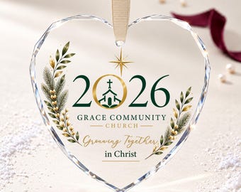 Puede incluir: Un adorno de cristal transparente en forma de corazón con borde facetado, colgado de una cinta beige. Incluye el texto 2026, Grace Community Church y Growing Together in Christ, junto a un icono de iglesia, una estrella y ramas botánicas.