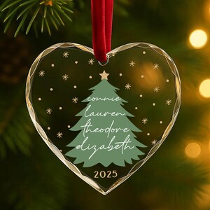 May include: Heart-shaped Christmas ornament with a green Christmas tree design and the names "Connie, Lauren, Theodore, Elizabeth" in white script. The year "2025" is printed at the bottom. The ornament hangs from a red ribbon.