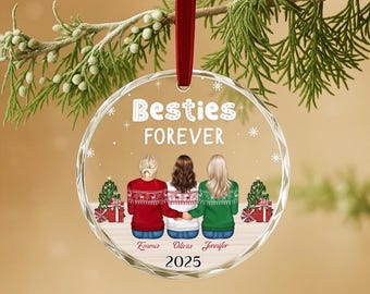 Può includere: Una decorazione natalizia rotonda in acrilico trasparente appesa a un nastro rosso. Il design mostra tre persone viste di spalle che indossano maglioni a motivi, con il testo Besties FOREVER, i nomi Emma, Olivia, Jennifer e l'anno 2025 stampati.