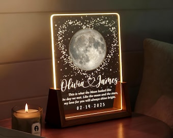 May include: A personalized night light with a full moon design and the names "Olivia & James" in elegant script. The light includes the date "02.14.2025" and a romantic quote. The wooden base and frame illuminate the acrylic panel.