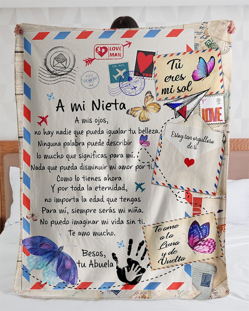 Puede incluir: Una manta blanca y beige con un diseño colorido con mariposas, corazones y aviones. La manta tiene un mensaje escrito a mano en español que dice 'A mi Nieta' e incluye el texto 'Tu eres mi sol' y 'Te amo a la Luna y de Vuelta'.