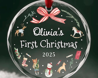 Könnte beinhalten: Ein klarer, runder Weihnachtsschmuck mit rotem Band. Der Schmuck zeigt den Text "Olivia's First Christmas 2025" und enthält Illustrationen eines Rentiers, Schaukelpferds, Schneemanns und anderer festlicher Elemente.