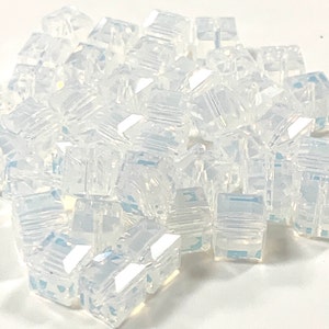 May include: A pile of clear iridescent glass cube beads. The beads are faceted and have a slight shimmer.