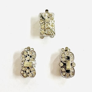 May include: Three silver-toned metal clasps with clear rhinestone embellishments. The clasps are designed for jewelry making and have a decorative, vintage style.