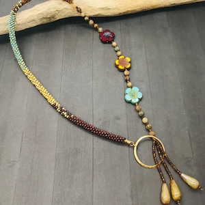 May include: A long beaded necklace with a gold ring pendant and three teardrop-shaped beads. The necklace features a graduated pattern of brown, yellow, and green beads, and four colourful flower-shaped beads.