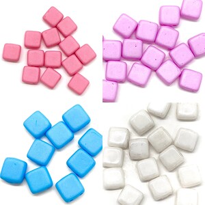 May include: Assortment of square glass beads in pink, blue, and white. The beads are opaque and have a matte finish.