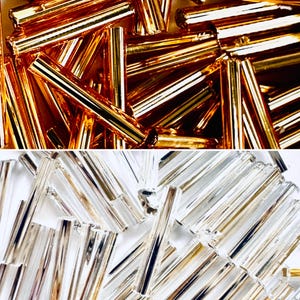 May include: Close-up of two sections of cylindrical beads. The top section features gold-colored beads, while the bottom section displays silver-colored beads. The beads are arranged in a scattered pattern, reflecting light and creating a textured appearance.