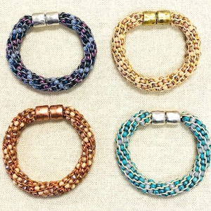 May include: Four beaded bracelets in different colours. One is blue and purple with silver clasps, another is tan and gold with gold clasps, a third is brown and copper with copper clasps, and the last is teal and grey with silver clasps.