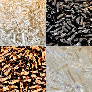 May include: Assortment of glass beads in various colors and finishes, including clear, iridescent, and metallic. The beads are arranged in four separate piles, showcasing their different textures and shapes.