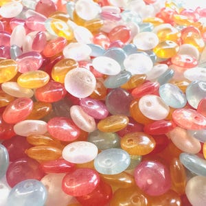 May include: A large pile of colorful, translucent, flat, round beads with a hole in the center. The beads are in shades of pink, orange, blue, and white.