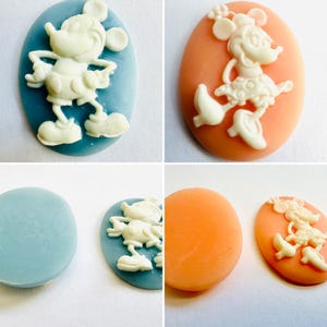 May include: Four oval-shaped cameo pendants featuring cartoon characters. Two pendants have a light blue background with Mickey Mouse, and two have an orange background with Minnie Mouse. The characters are in white.