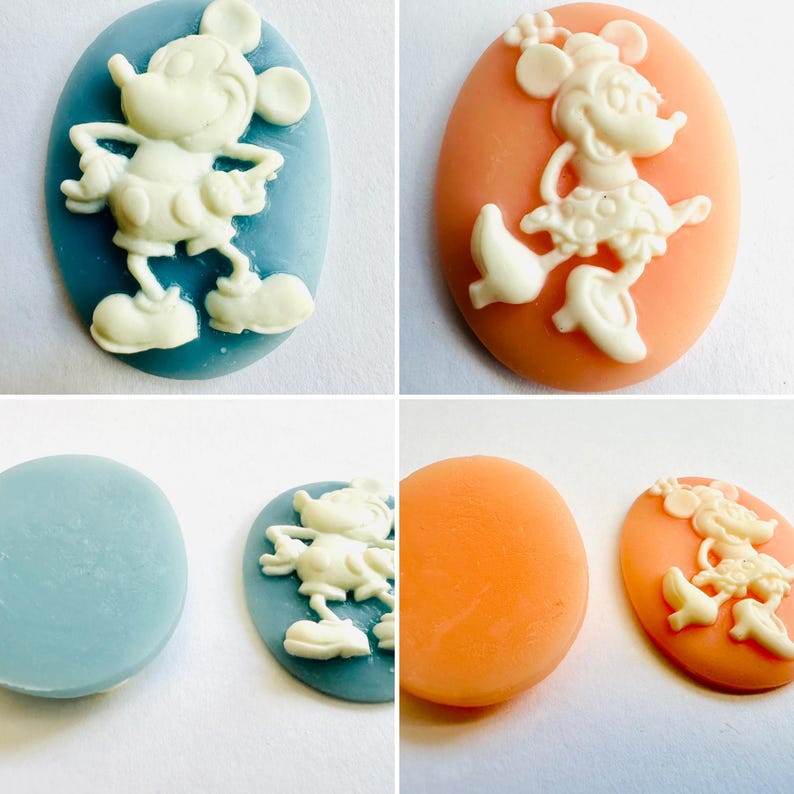 May include: Four oval-shaped cameo pendants featuring cartoon characters. Two pendants have a light blue background with Mickey Mouse, and two have an orange background with Minnie Mouse. The characters are in white.