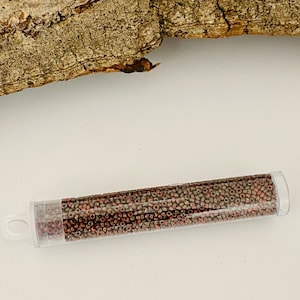 May include: A clear plastic tube filled with small, round, copper-coloured beads. The beads have a metallic sheen and are arranged in a random pattern.