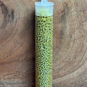 May include: A clear plastic tube filled with small, gold-colored beads. The tube has a white cap with a loop handle.