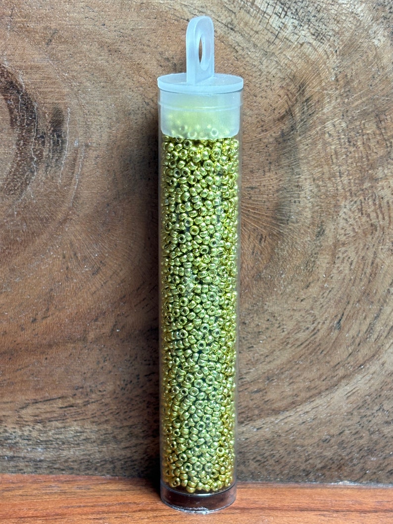 May include: A clear plastic tube filled with small, gold-colored beads. The tube has a white cap with a loop handle.