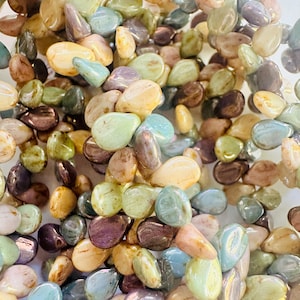 May include: A strand of iridescent, multi-colored, glass beads in a teardrop shape. The beads have a mottled, textured surface and are arranged in a loose pile.
