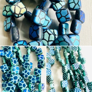 May include: An assortment of square and rounded beads in shades of blue and teal. The beads have a geometric pattern in a darker blue. Some beads are strung together, while others are loose, suggesting jewelry making supplies.