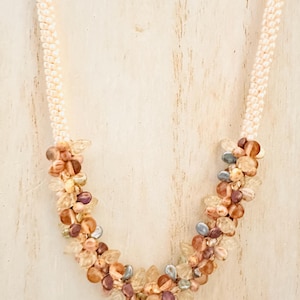May include: A delicate necklace with a cream-colored beaded chain and a cluster of small, multi-colored beads in shades of brown, pink, and purple.