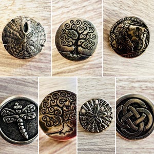 May include: A collection of silver-toned metal buttons with various designs. The buttons feature a sand dollar, a tree of life, a buffalo, a dragonfly, and Celtic knot patterns. These buttons are likely used for sewing or crafting.