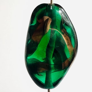 May include: A translucent, teardrop-shaped bead with a dark green base and swirling patterns of lighter green and gold. The bead is suspended by a thin, silver-colored wire, showcasing its unique, organic design. This bead is suitable for jewelry making.
