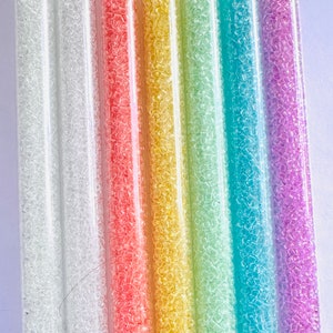 May include: Seven clear plastic tubes filled with iridescent seed beads in a rainbow color gradient. The colors are white, pink, yellow, green, blue, and purple.
