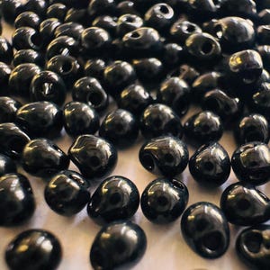 May include: A large pile of black teardrop-shaped beads. The beads are smooth and shiny.