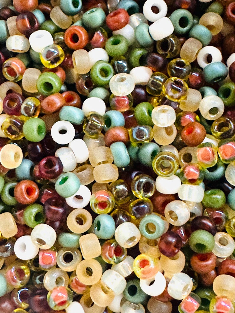 May include: A large assortment of small, round glass beads in various colors, including brown, green, white, and yellow. The beads are perfect for jewelry making or other craft projects.