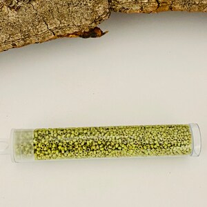 May include: A clear plastic tube filled with small, light green glass beads. The tube is lying on a white surface.