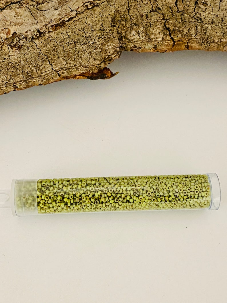 May include: A clear plastic tube filled with small, light green glass beads. The tube is lying on a white surface.
