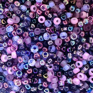 May include: A close-up of a large assortment of small, round beads in shades of purple, pink, and blue. The beads are made of glass and have a variety of finishes, including iridescent, matte, and clear.