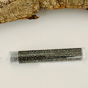 May include: A clear plastic tube filled with small, round, dark grey beads. The beads have a metallic sheen.