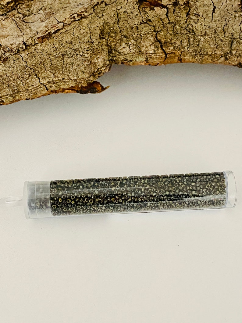 May include: A clear plastic tube filled with small, round, dark grey beads. The beads have a metallic sheen.