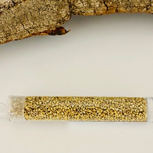 May include: A clear plastic tube filled with small, round, light beige seed beads.