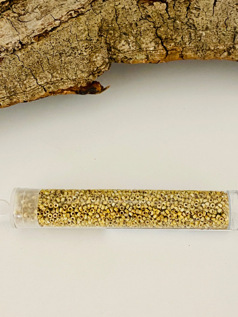 May include: A clear plastic tube filled with small, round, light beige seed beads.