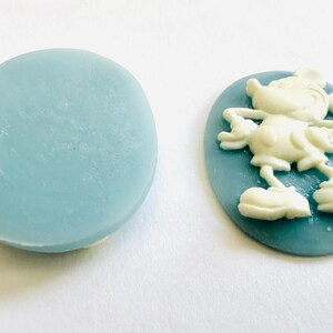 May include: Two light blue oval-shaped soap bars. One is plain, the other features a white Mickey Mouse cameo design. The soap bars are likely handmade and suitable for decorative or practical use.