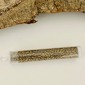 May include: A clear plastic tube filled with small, gold-coloured seed beads. The tube has a white cap on one end and a clear cap on the other end.