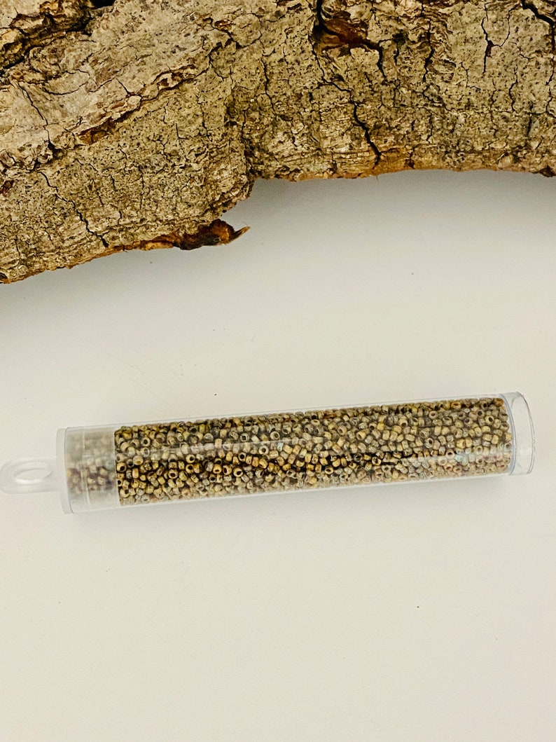 May include: A clear plastic tube filled with small, gold-coloured seed beads. The tube has a white cap on one end and a clear cap on the other end.