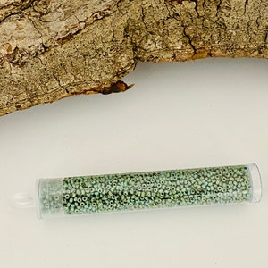 May include: A clear plastic tube filled with small, light green glass beads. The tube is lying on a white surface.