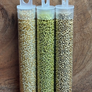 May include: Three clear plastic tubes filled with gold, silver, and bronze seed beads. The tubes have a clear plastic handle at the top.