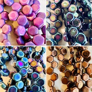 May include: Assortment of iridescent glass hexagon beads in purple, blue, and brown colors. The beads are arranged in a random pattern.