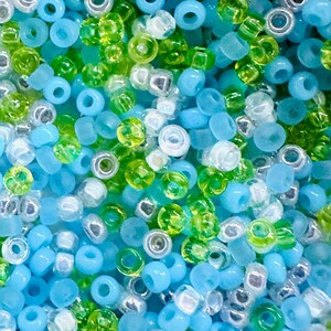 May include: A close-up of a variety of small, round beads in shades of blue, green, and white. The beads are arranged in a random pattern, creating a colorful and textured background.