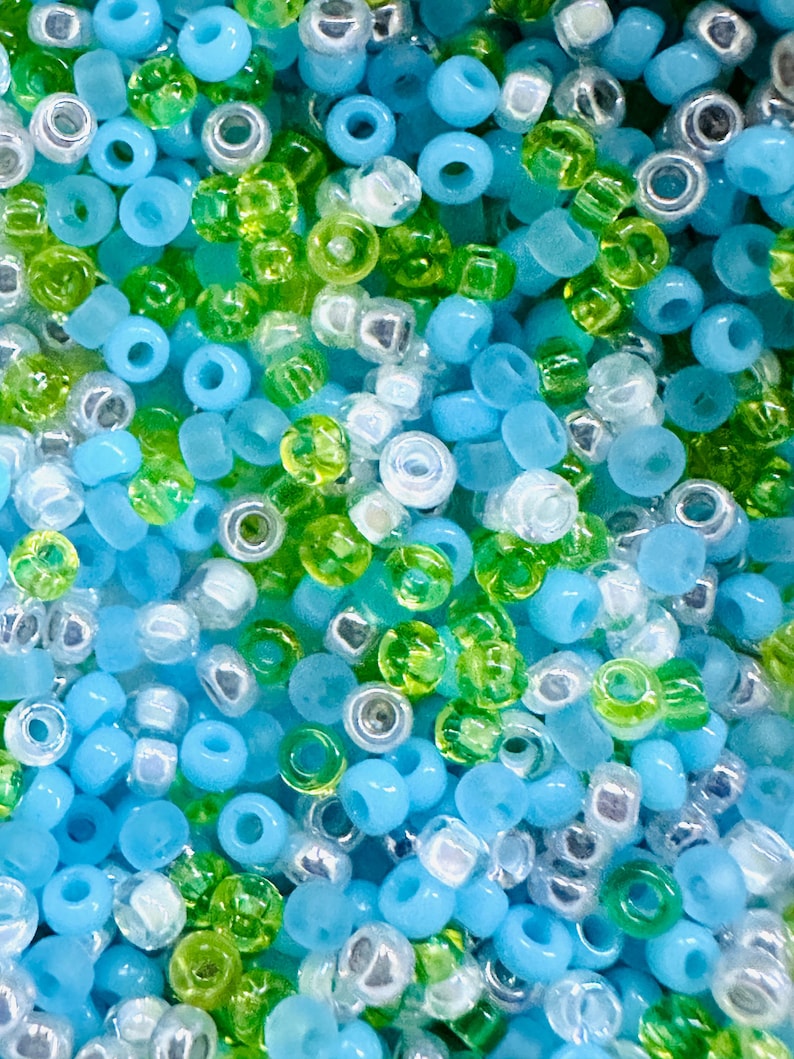 May include: A close-up of a variety of small, round beads in shades of blue, green, and white. The beads are arranged in a random pattern, creating a colorful and textured background.