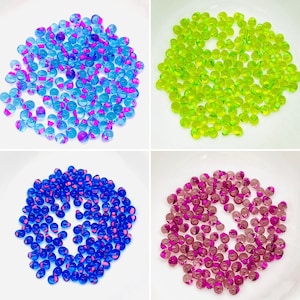 May include: Four piles of colorful glass beads. The beads are translucent and have a speckled pattern. The beads are arranged in a square pattern on a white background.
