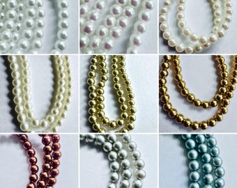 May include: A collection of nine strands of round beads in various colors including white, cream, gold, bronze, silver, and light blue. Each strand features uniform spherical beads arranged in vertical lines against a plain background.
