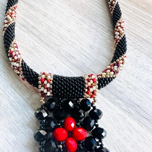 May include: A black beaded necklace with a red and white geometric pattern. The necklace has a black and red beaded pendant.