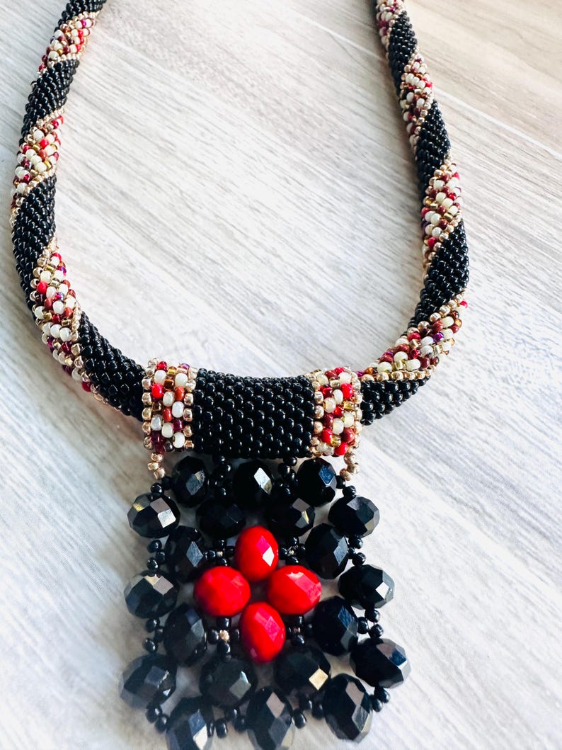 May include: A black beaded necklace with a red and white geometric pattern. The necklace has a black and red beaded pendant.